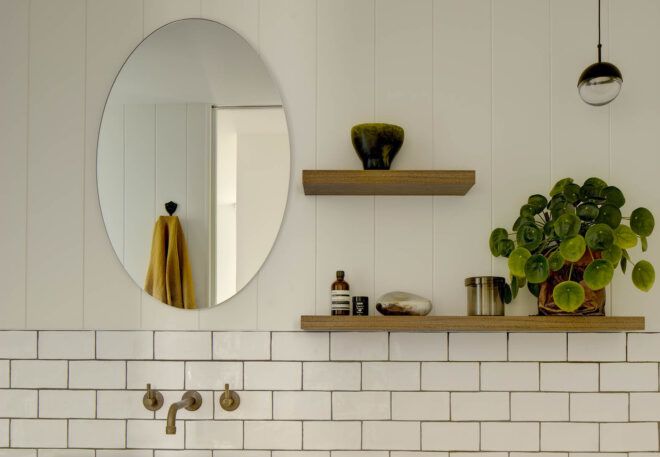 A white bathroom with an oval-shaped mirror and shelves built into the wall.