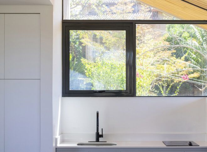 A kitchen with white counters and cabinets. Above the sink is a square, sliding glass window.