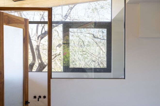 A frosted glass door with wood frame leads into a bathroom with large windows.