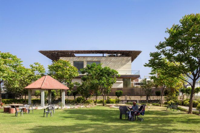 A green yard with a family lounging on it in front of a home with a stone facade and overhanging roof.