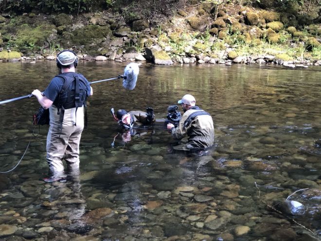 A person holds a boom mic over a person in snorkeling equipment while a third person films them.