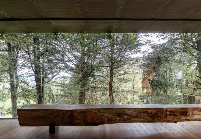 A log bench across from floor-to-ceiling windows that look out on a forest.
