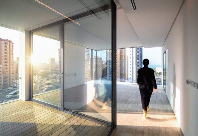 A person walking on a balcony that wraps around a glass wall.