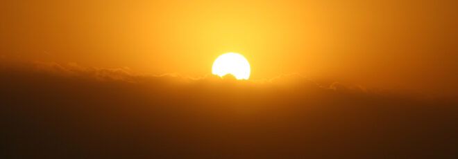 A sun rising behind clouds in a hazy sky.
