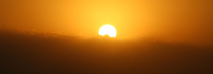 A sun rising behind clouds in a hazy sky.