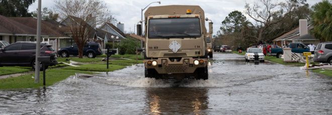 A large brown truck driving through a flooded residential street.