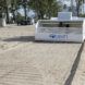 A small white robot with wheels and a 4ocean logo on it sweeps a beach for plastic waste.
