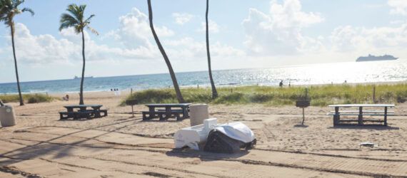 A small white robot with wheels on a beach.