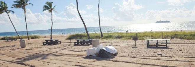 A small white robot with wheels on a beach.