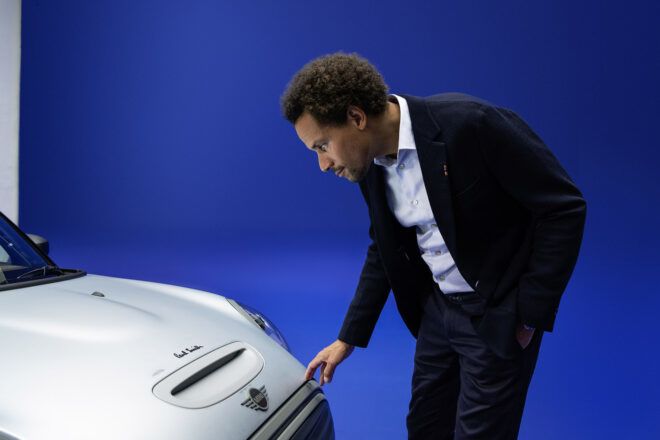 A person touching the hood of a silver and black car on a blue platform.