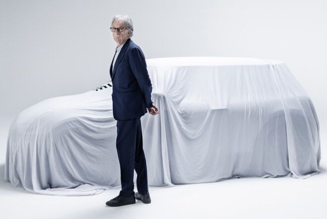 A person in a suit standing next to a car covered in a white cloth.