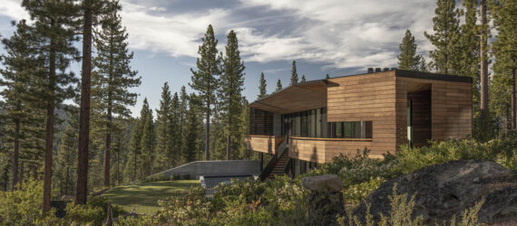 A landscape view of a home with wood siding surrounded by a forest.