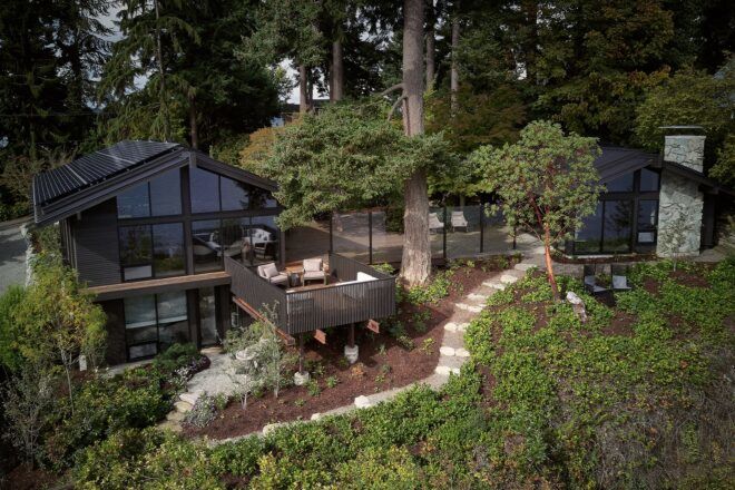 An overhead view of Loom House, showing two structures connected via a patio/bridge. A stone path leads from one structure through the garden to the left.