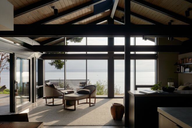 A sitting room with two off-white chairs and a matching coffee table. Floor-to-ceiling windows look out onto the Puget Sound.