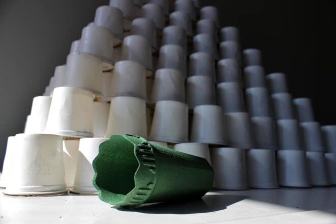 A green cone-like device in front of a tower of coffee pods.