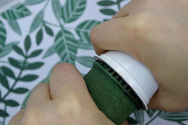 A pair of hands gripping a green device that is separting the parts of a coffee pod.