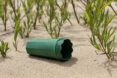 A green cone-like device laying in the sand in front of a patch of plants.