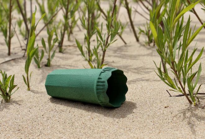 A green cone-like device laying in the sand in front of a patch of plants.
