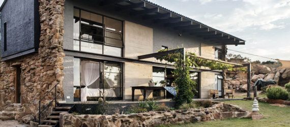 A two-level home with stone accents, large windows and a patio leading to a green lawn.
