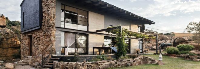 A two-level home with stone accents, large windows and a patio leading to a green lawn.