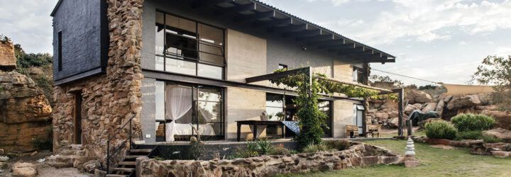 A two-level home with stone accents, large windows and a patio leading to a green lawn.