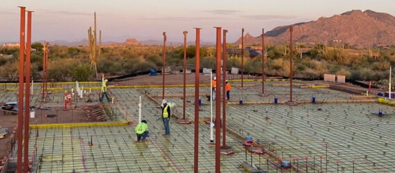 People working on the foundation of a construction site, with mountains in the background.