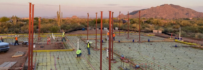 People working on the foundation of a construction site, with mountains in the background.