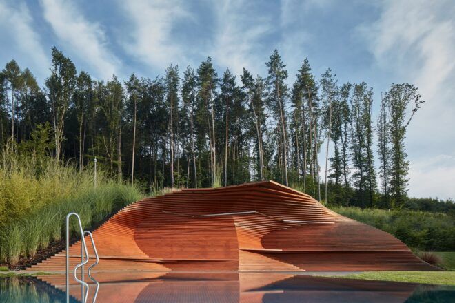 A swimming pool with a wavy, triangular wood structure built over one corner.