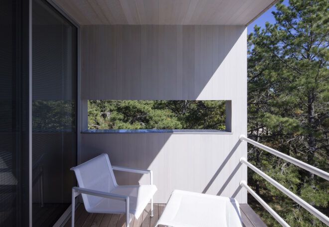 A balcony with a white deck chair overlooking a forest.