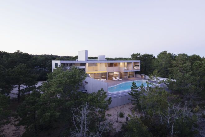 A view of the entire residence, showing a pool in front of a long, rectangular two-level home.