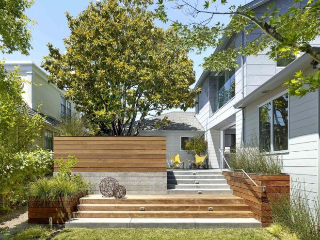 A green yard sits in front of wood and concrete steps that lead up to a house.