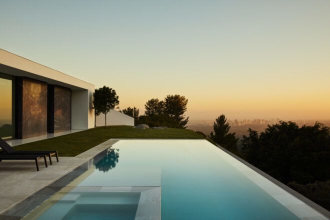 House at sunset with an infinity pool overlooking a city.
