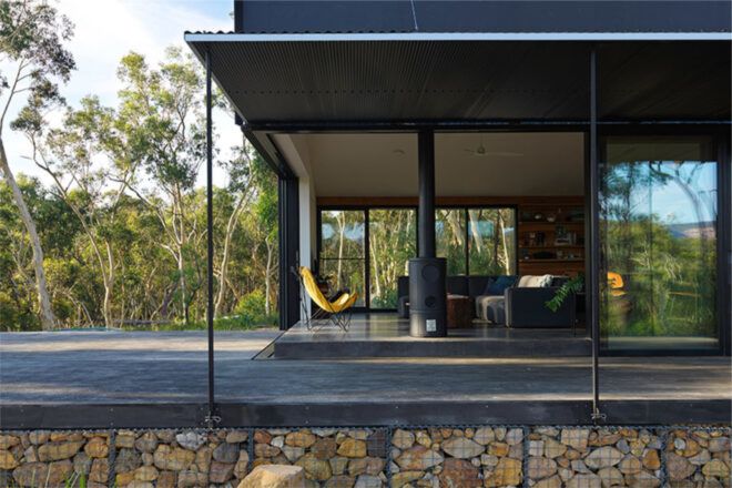 A single-level cabin with a roof over a gray patio that borders a forest.