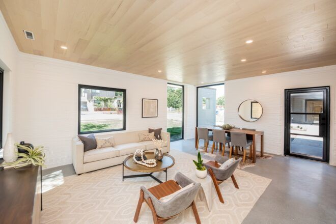 A neutral living area with white walls, a white rug, wood ceilings, a white sofa and gray chairs.