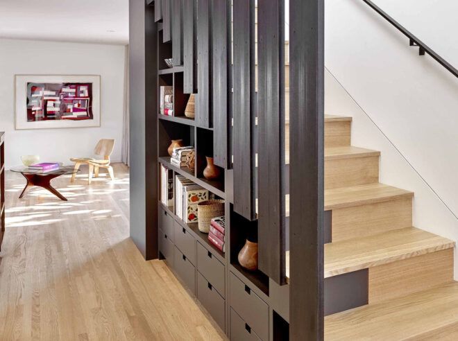 Wood floors lead from a sitting room to a stairwell with gray railings that double as cabinets.