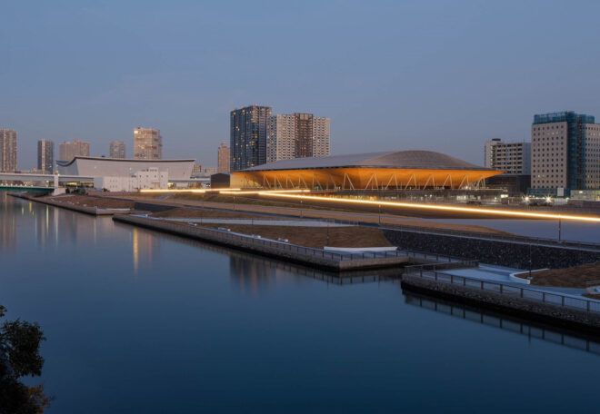 A long, lit-up structure on the bank of a lake.
