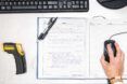 A work desk with a yellow and black tool, a notebook and a hand holding a computer mouse.