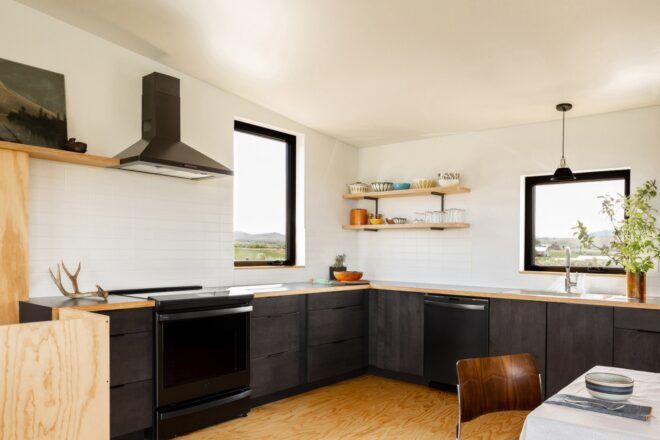 A kitchen with black counters and appliances and white walls.