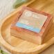 An orange-pink bar of soap on a wood dish.