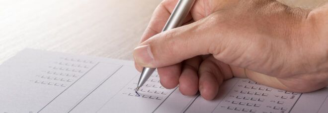 A hand holding a pen to fill out a ballot.
