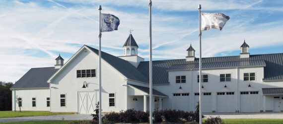 A landscape shot of a white building with three flagpoles in front of it.