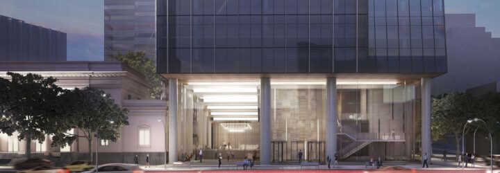 A long exposure shot of the street in front of an office tower lit up on the ground floor, with glass walls.