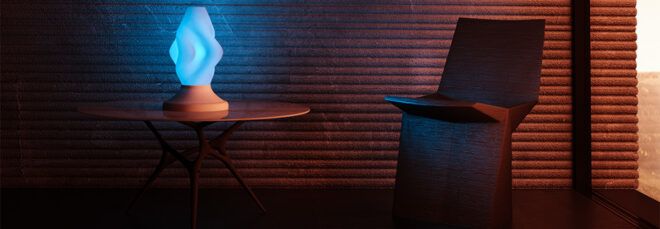 A blue lamp glowing on an end table in a dark room next to a chair.