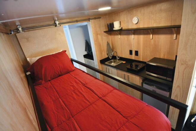A red bed next to a kitchenette inside a tiny home.