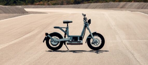 A sideview of an electric moped parked on a dusty road.