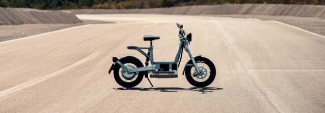 A sideview of an electric moped parked on a dusty road.