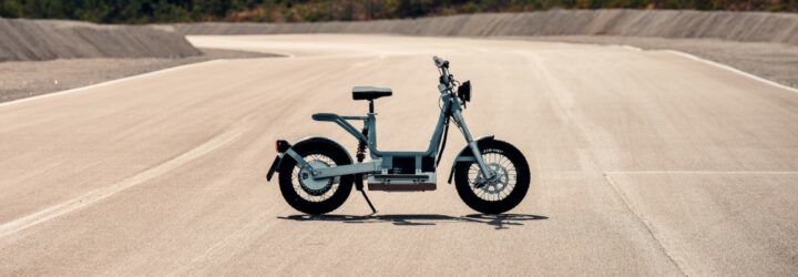 A sideview of an electric moped parked on a dusty road.