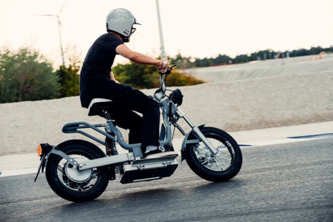 A sideview of a person wearing a helmet and driving an electric moped.