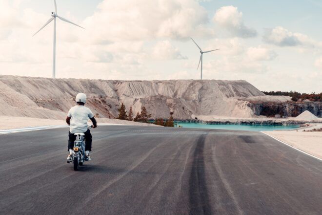 The back of a person riding a moped, with windmills in the distance.