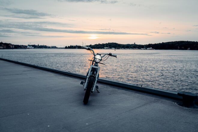 The front of an electric moped parked on a dock by the water.